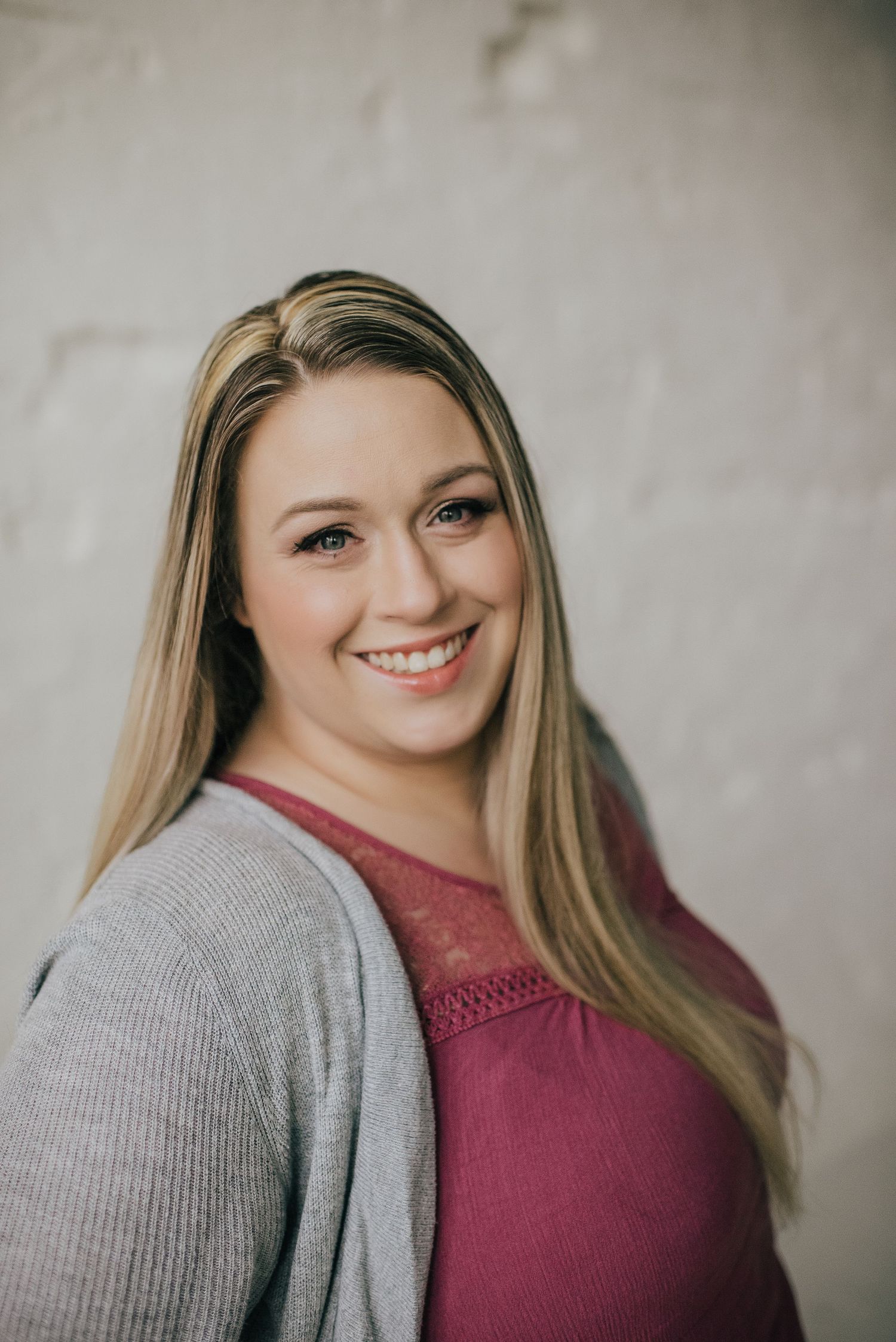 Professional headshot of woman in grey cardigan and burgundy top against neutral background.