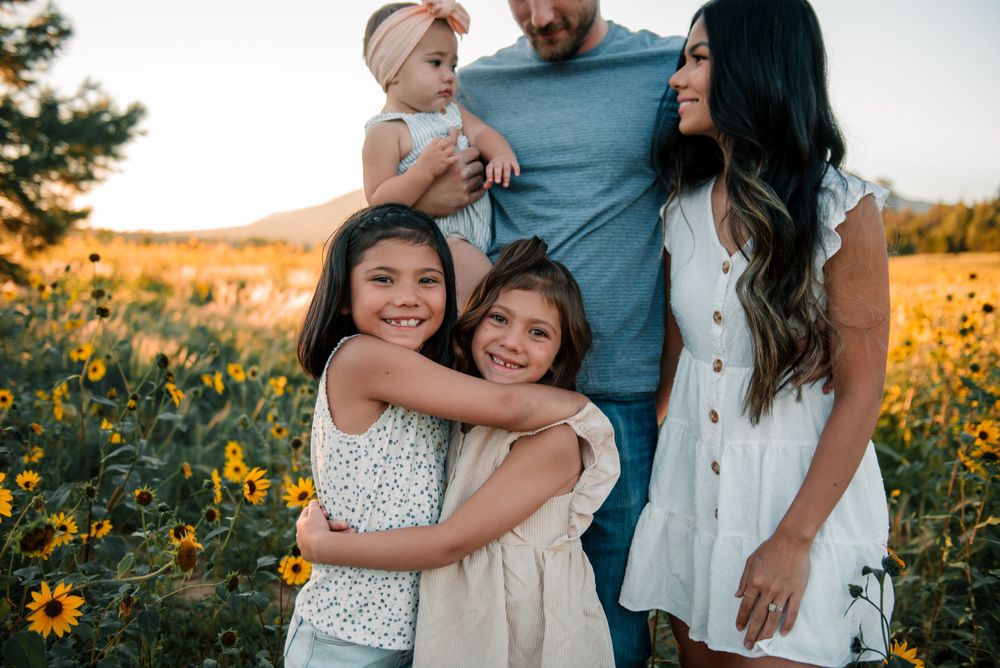 Loving family moment captured in a field of yellow sunflowers with mountains in the distance.