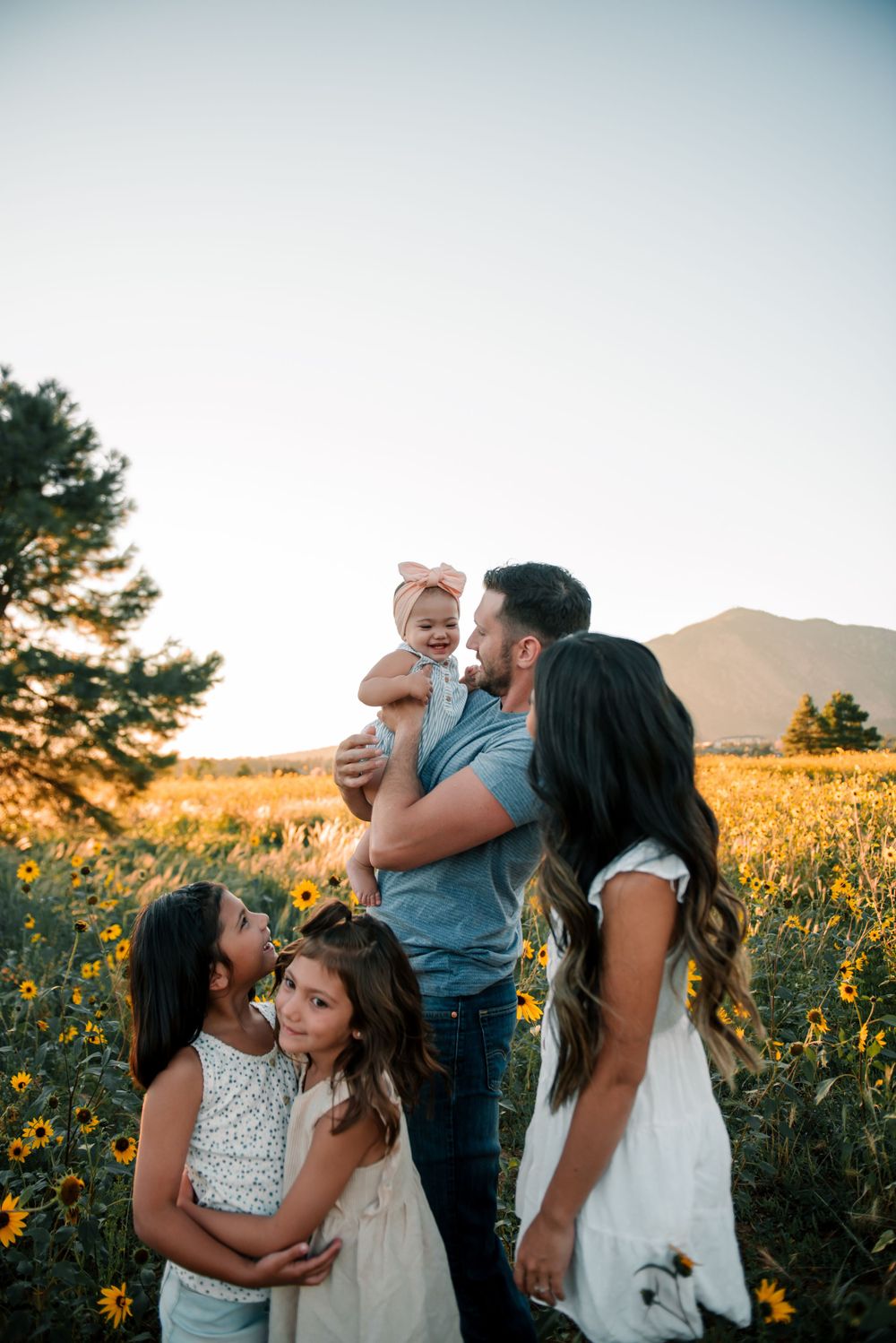 Candid family photo in a sunflower field during golden hour with mountain scenery.