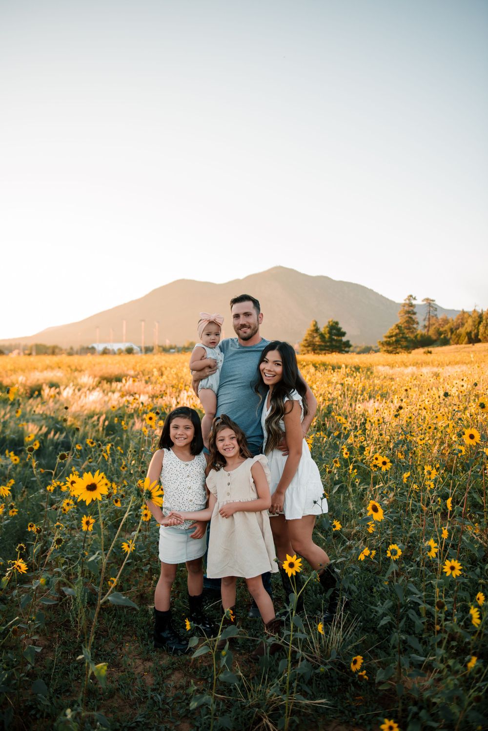 Family portrait amidst blooming sunflowers with mountain vista during golden hour.