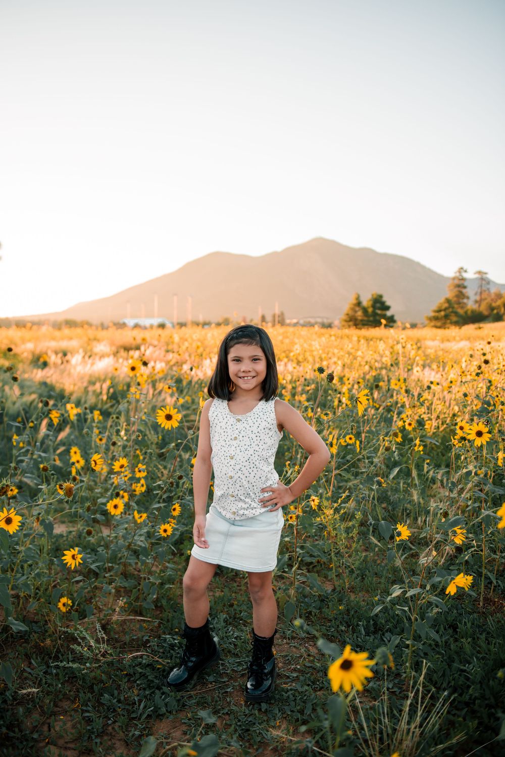 A child in a polka dot top dances through a field of sunflowers with mountains in the background.