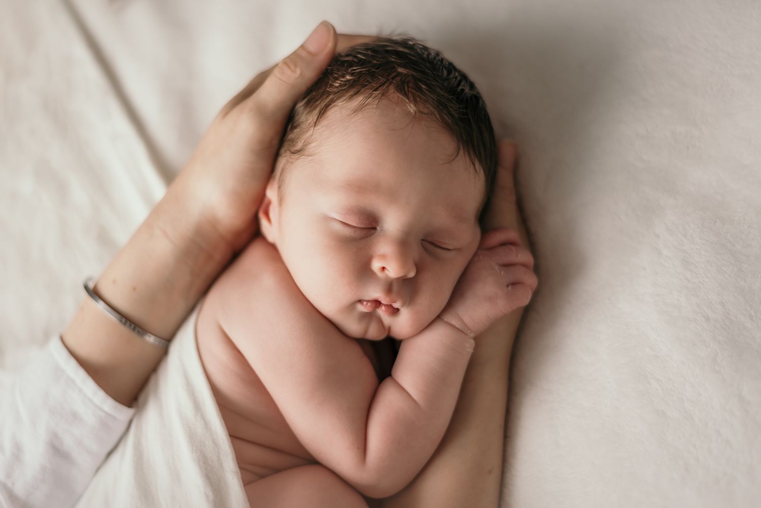 Peaceful newborn baby sleeping on white fabric with hands near face.