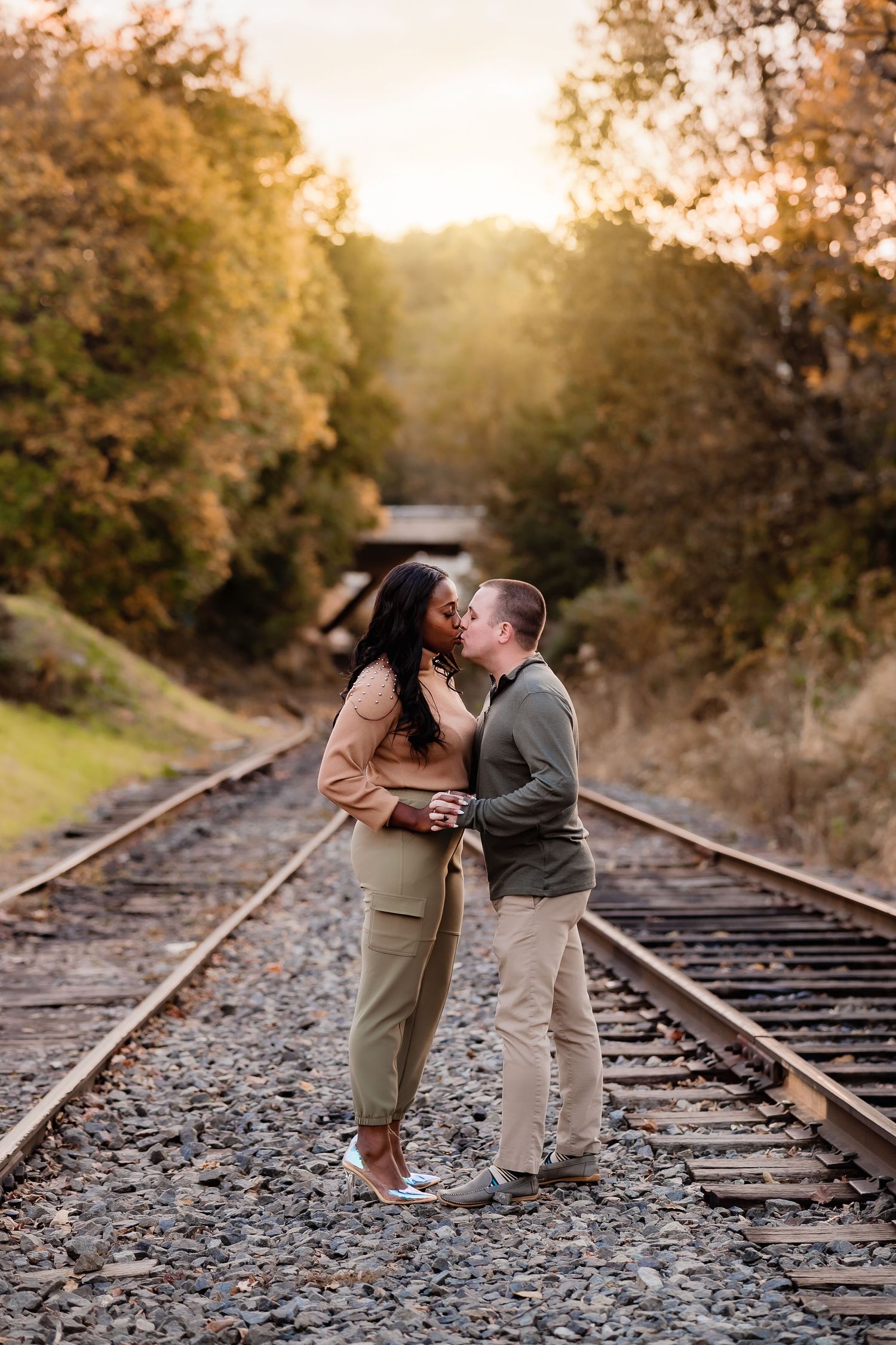 Couple embracing on train tracks during sunset in autumn setting.