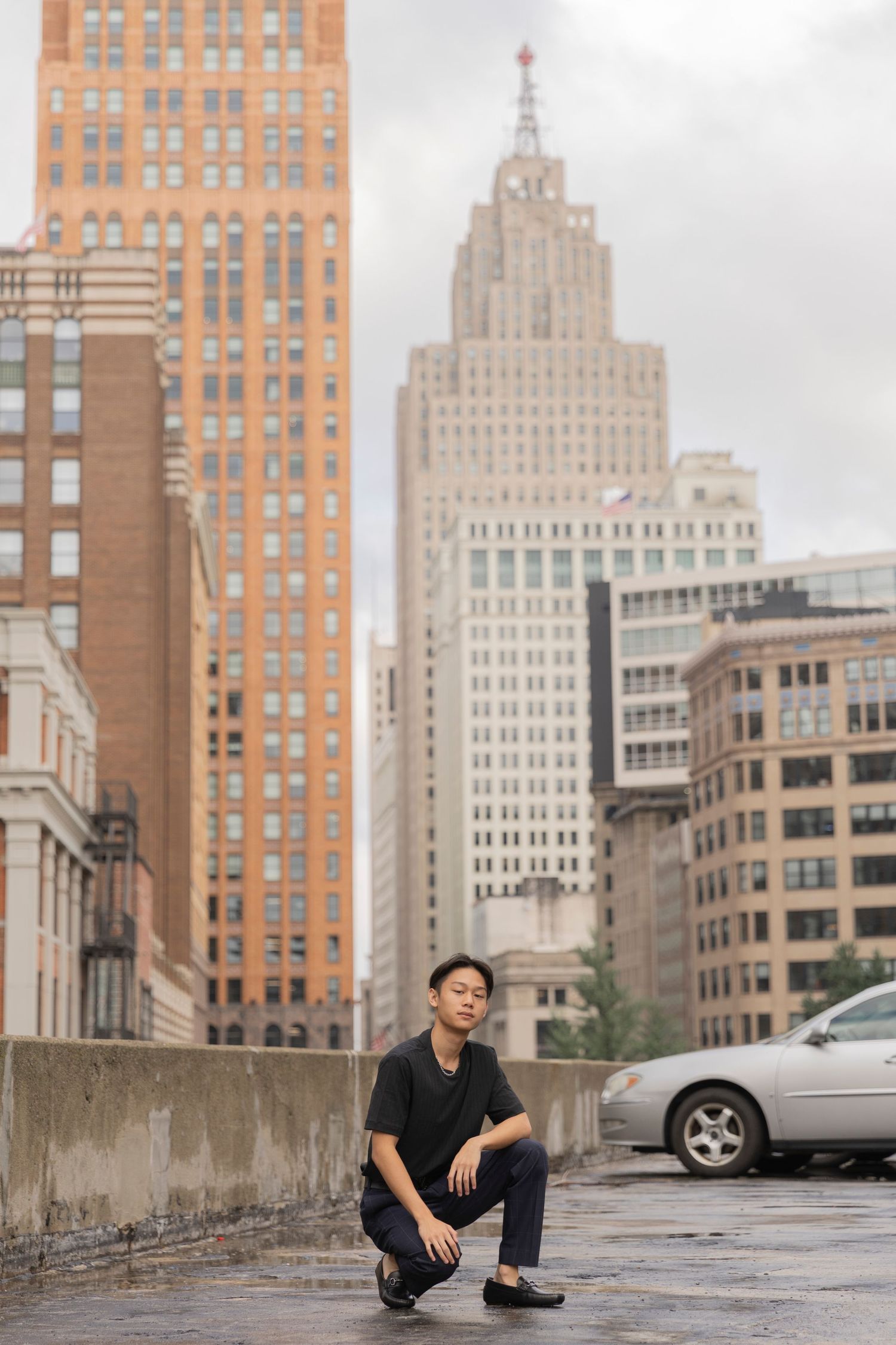 teenage boy squatting to pose for senior photos on a rooftop in Downtown Detroit