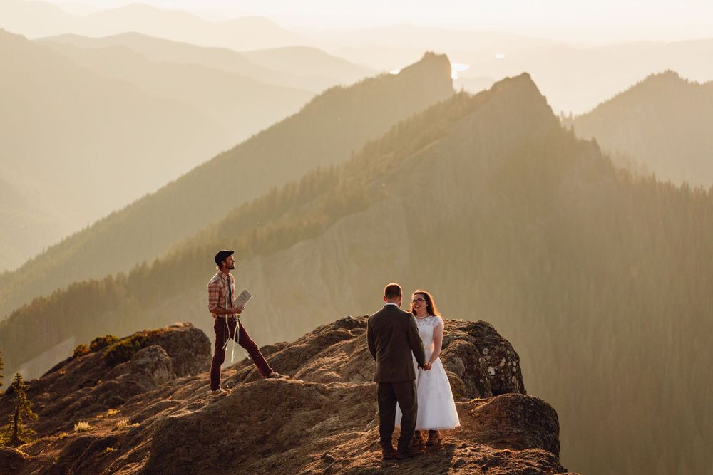 Couple exchanges vows with an officiant on a dramatic mountain summit bathed in golden hour light.