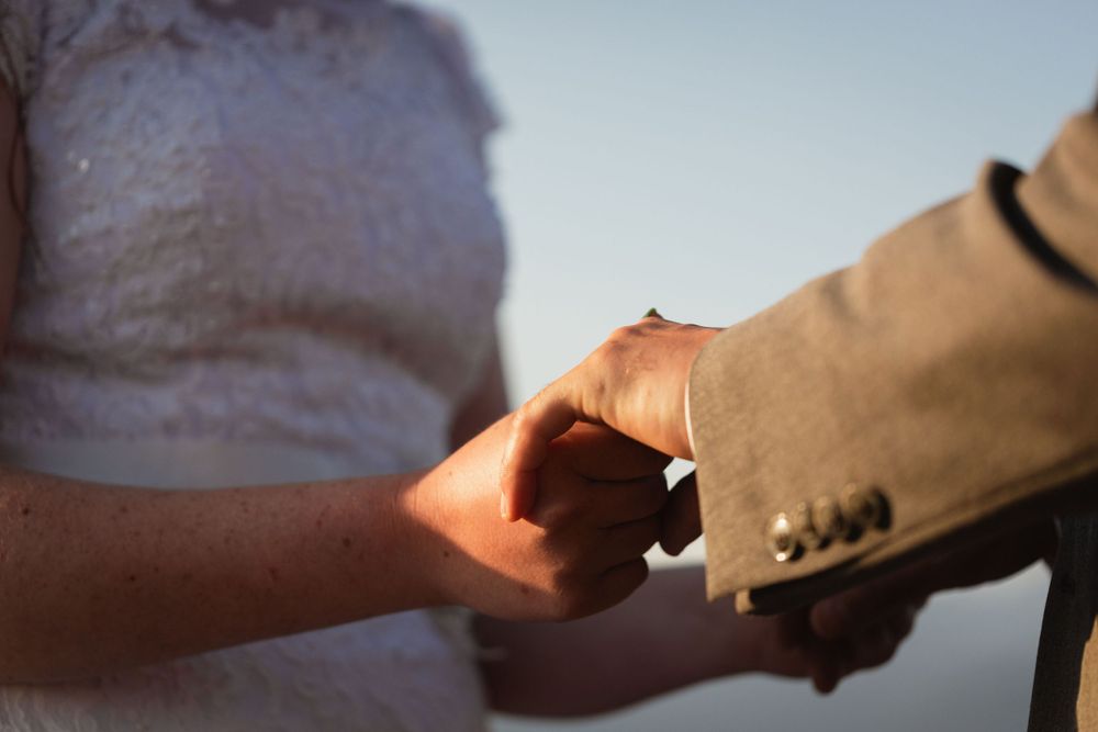 Close-up of bride and groom holding hands during outdoor wedding ceremony in warm sunlight.