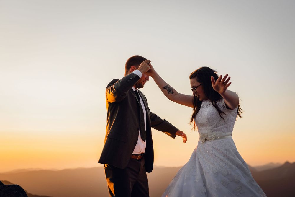 Groom spins bride in a lace wedding dress during a romantic sunset mountain elopement dance.