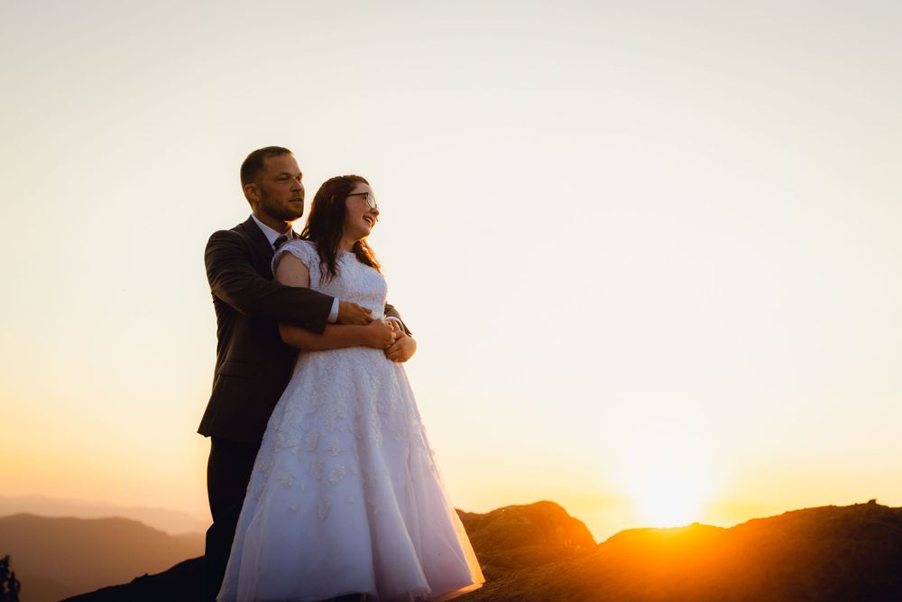Bride and groom embracing on a mountain summit during a golden sunset wedding photo.