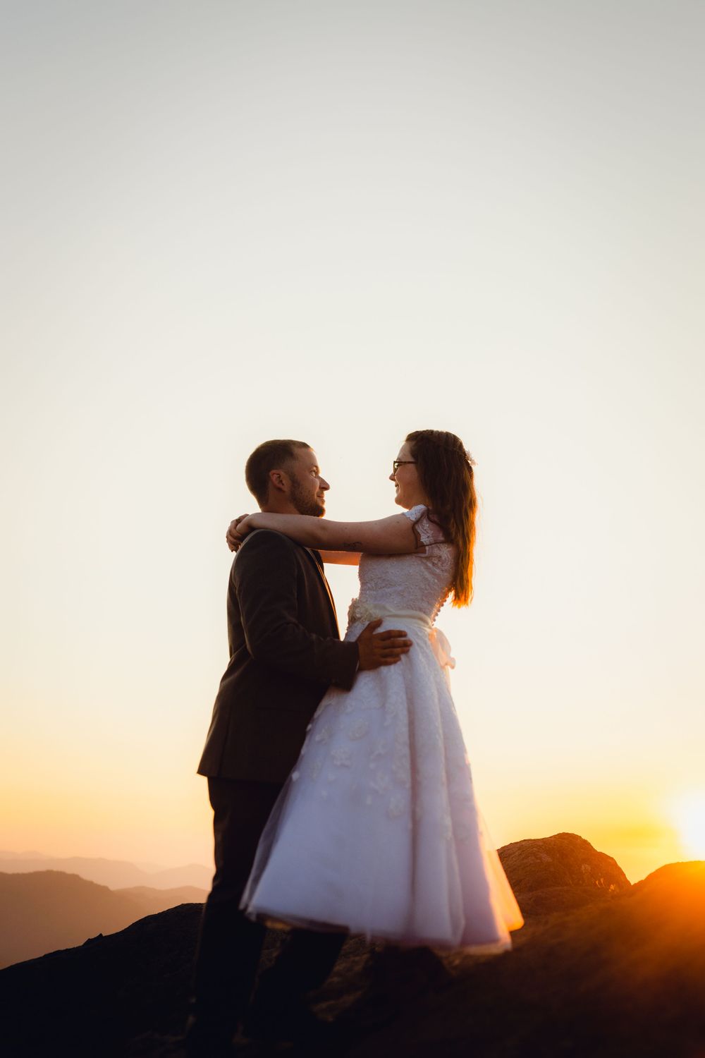 Wedding couple facing each other tenderly on a rocky mountaintop at sunset.