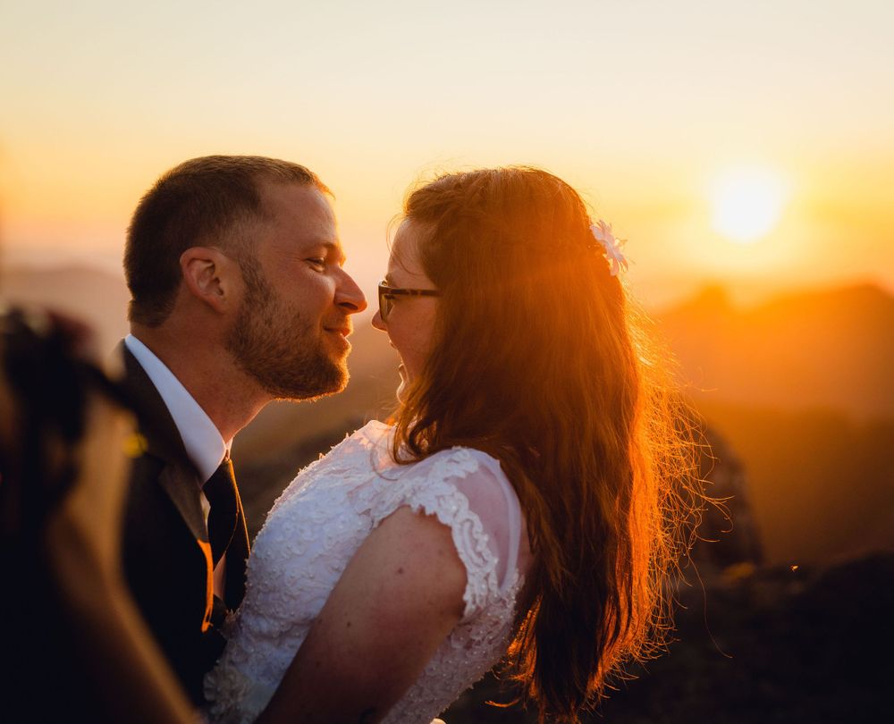 Bride and groom sharing an intimate moment backlit by a warm glowing sunset.