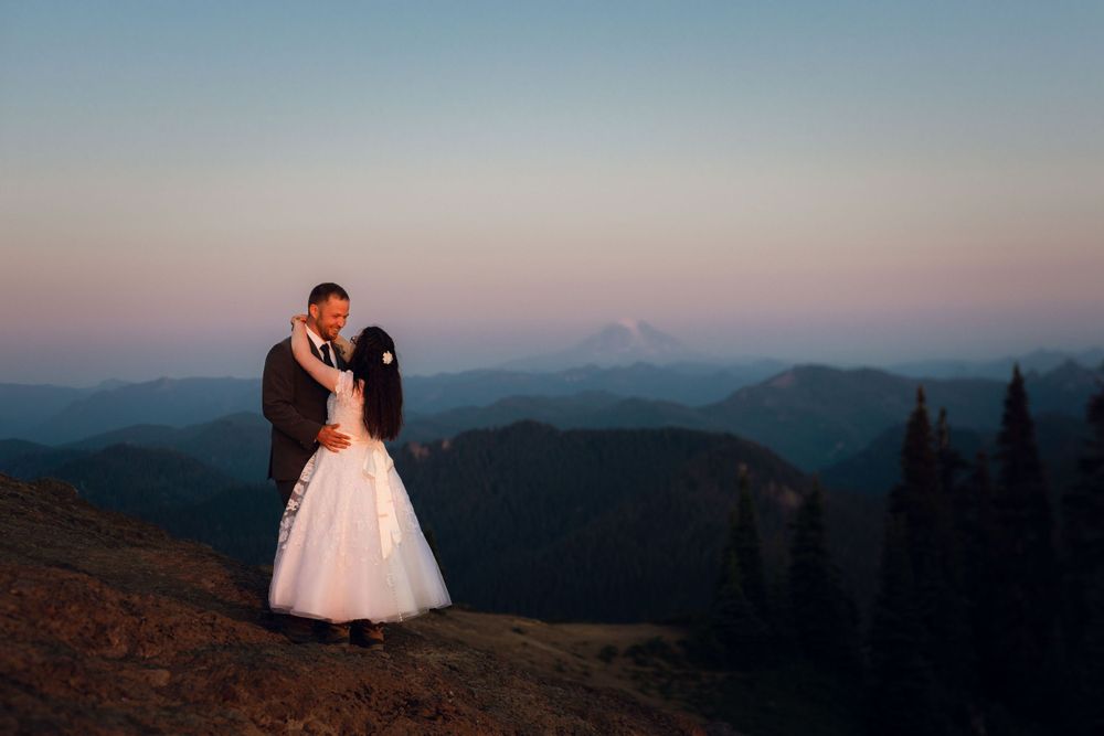 Bride and groom kissing on a mountaintop at twilight with misty mountain backdrop.
