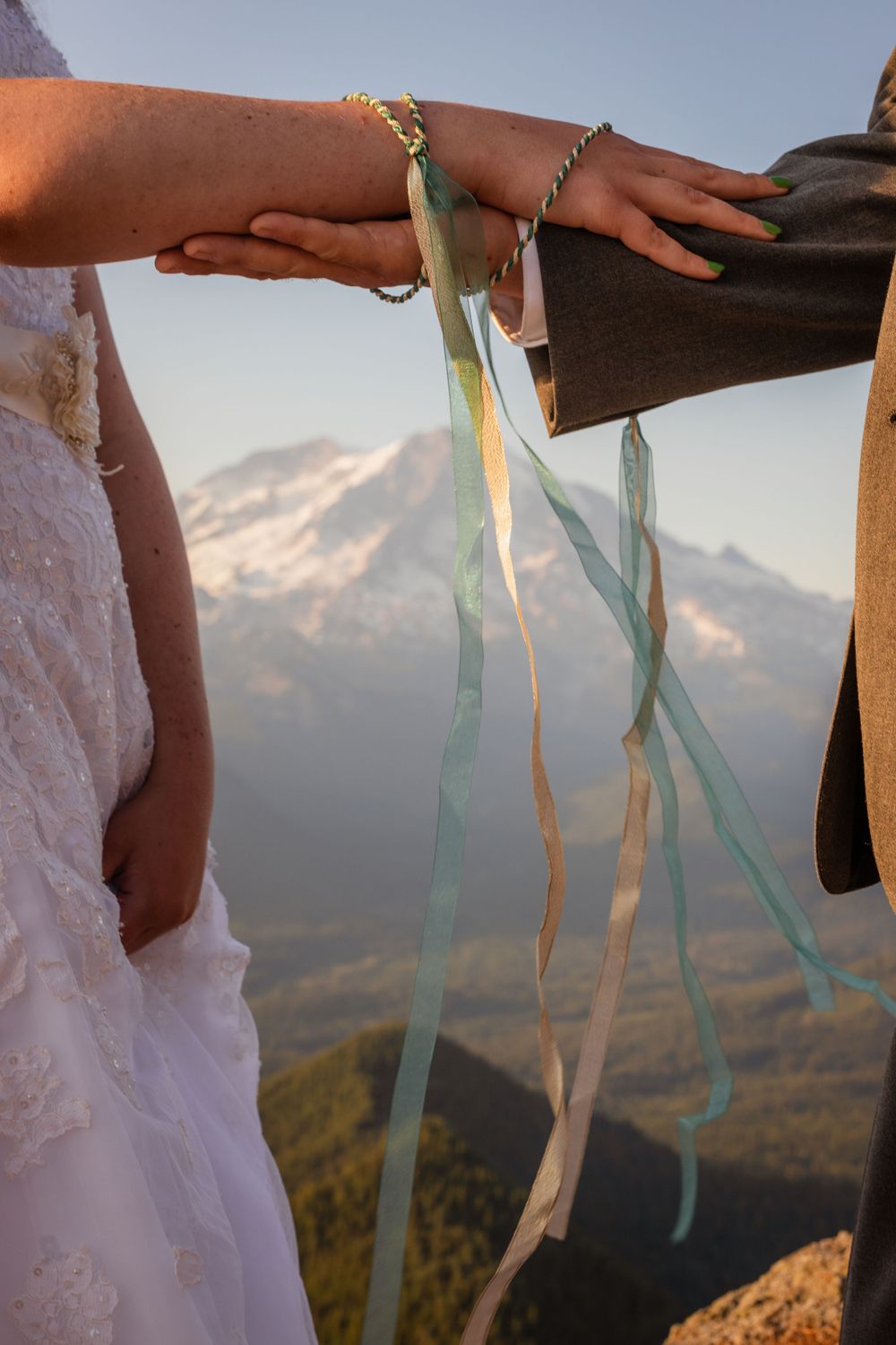 Close-up of handfasting ceremony with colorful ribbons binding couple's hands with snowy mountain backdrop.