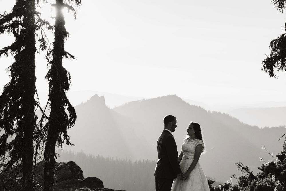Bride and groom standing together on a misty mountain overlook in black and white.