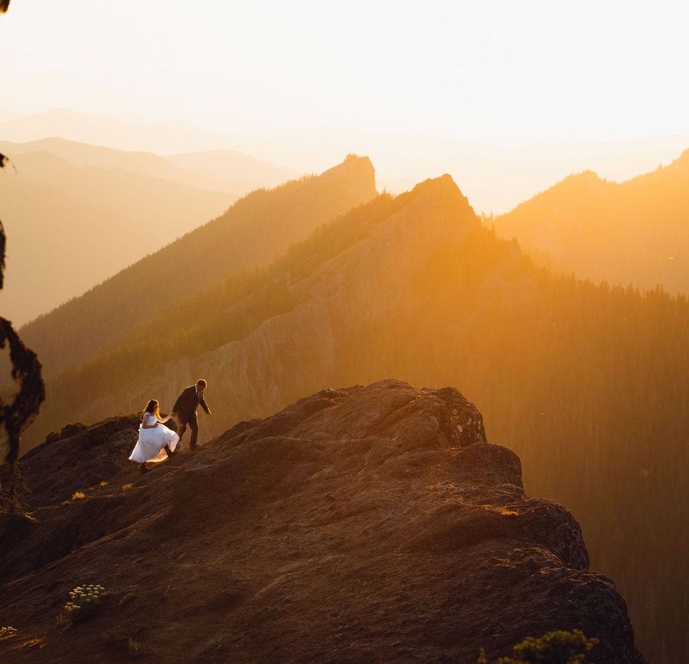 Bride and groom exploring a rugged mountain peak bathed in warm golden sunset light.