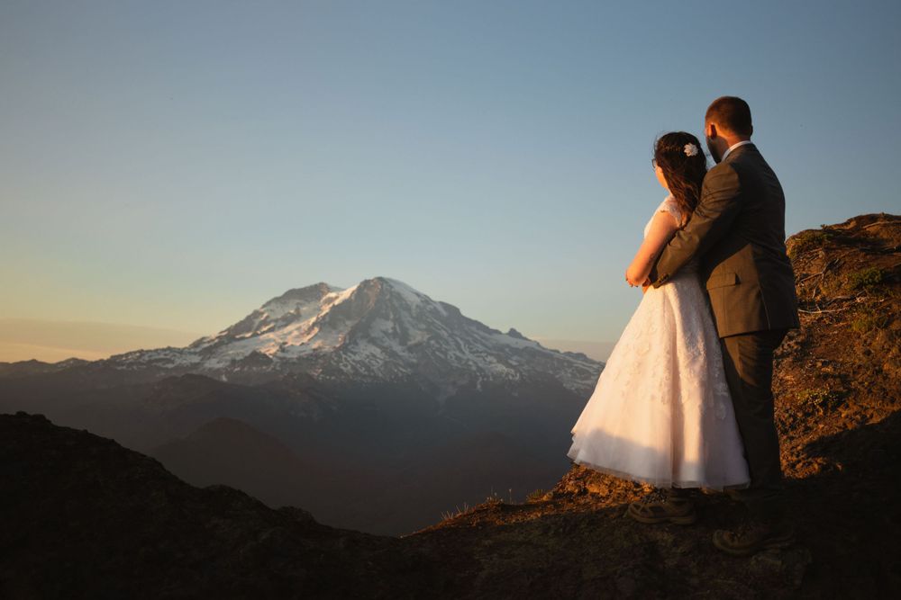 Bride and groom embracing while overlooking snow-capped Mount Rainier at sunset.