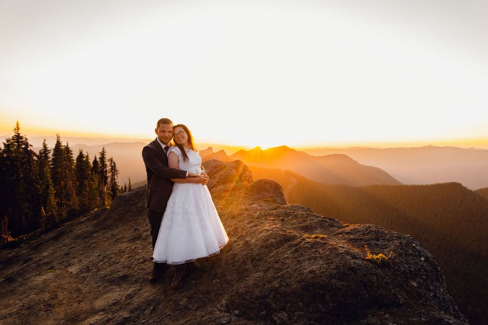 Bride and groom embracing on a rocky mountaintop during a breathtaking golden sunset.
