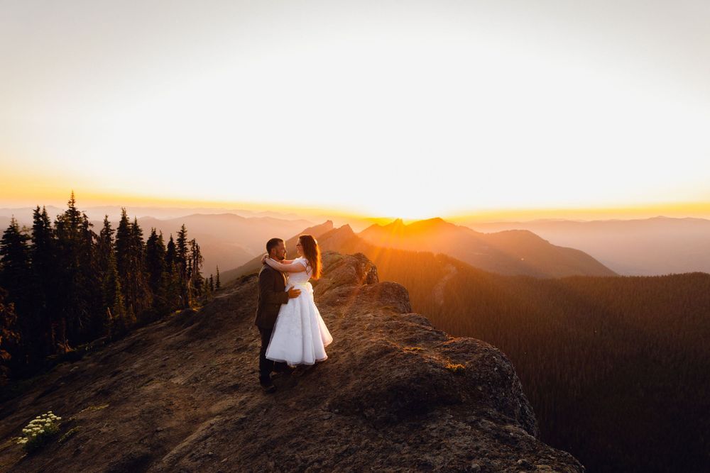 Bride and groom share a kiss on rocky mountain peak during dramatic golden hour sunset.