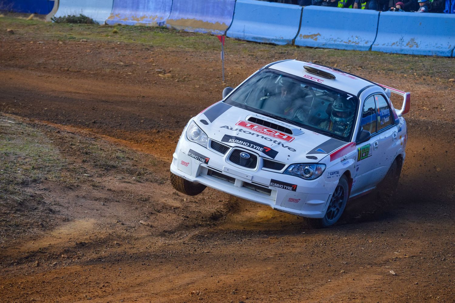 White rally car slides through dirt corner during competitive race.