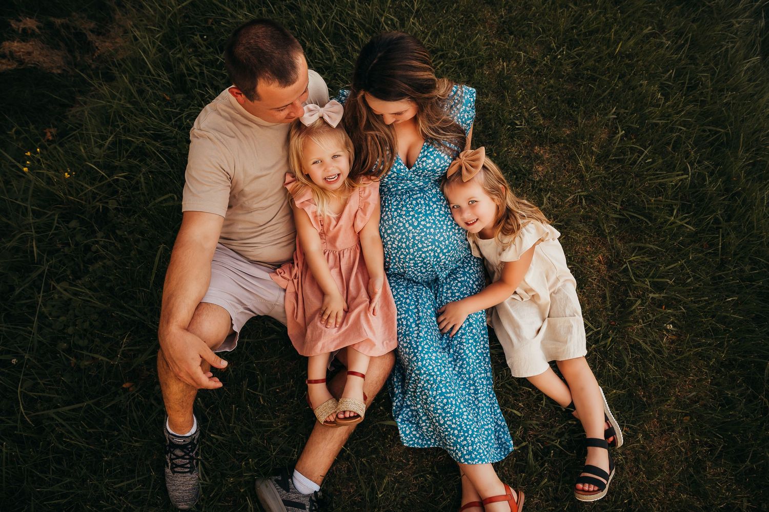 An overhead view of a happy family of four lying together on grass during a summer photo session.