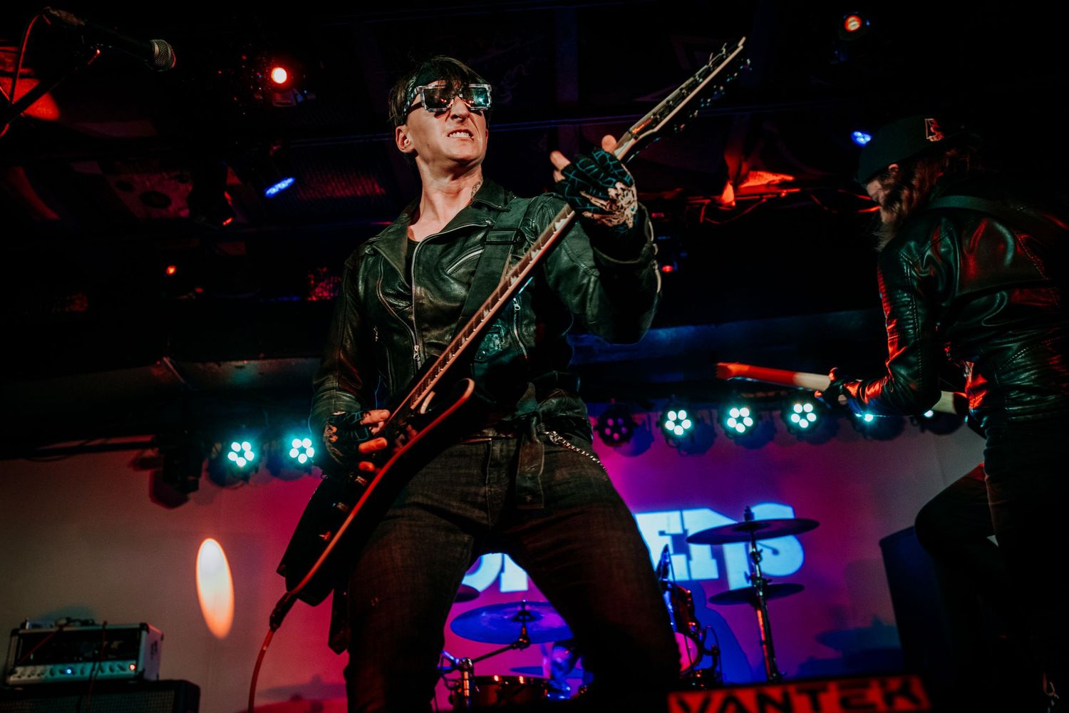 Performer plays electric guitar under colorful stage lights at rock concert.