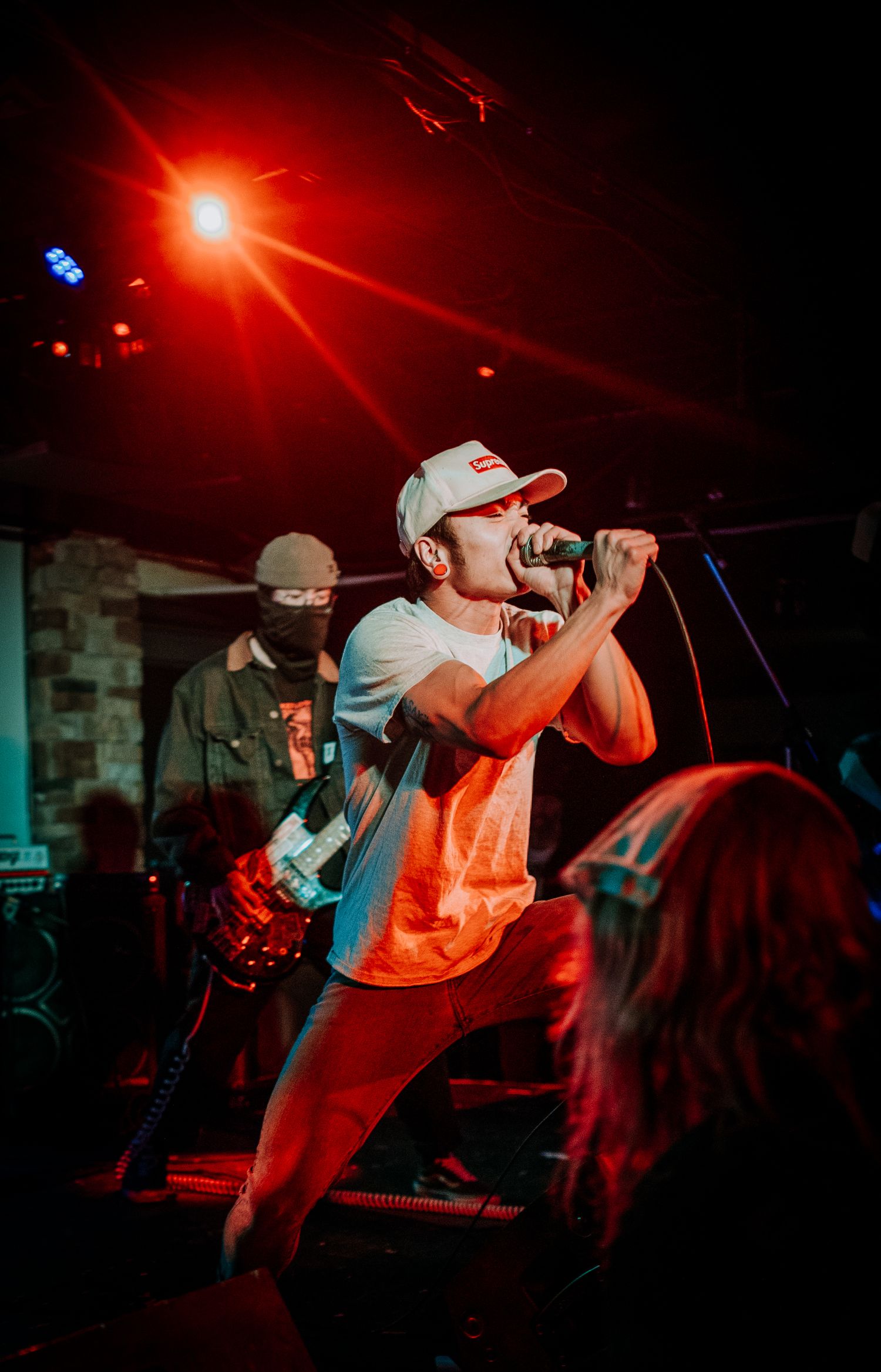 Lead singer performs energetically under red stage lighting with bassist in background.