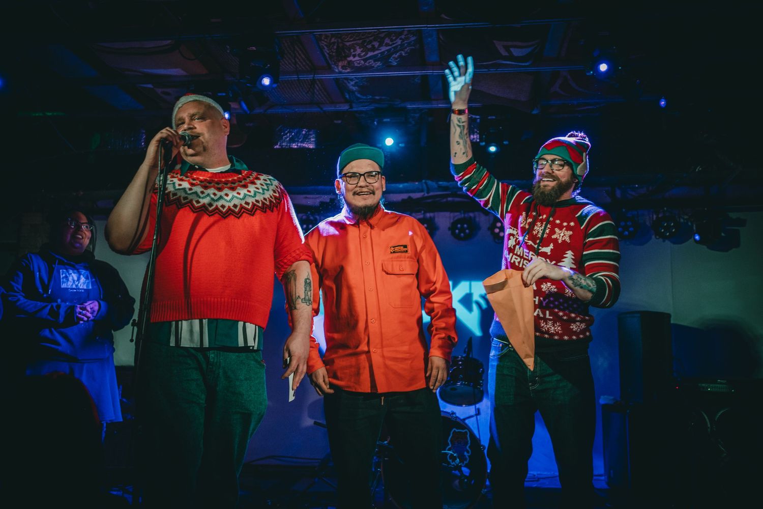 Three performers in festive winter attire entertaining on stage with blue lighting effects.