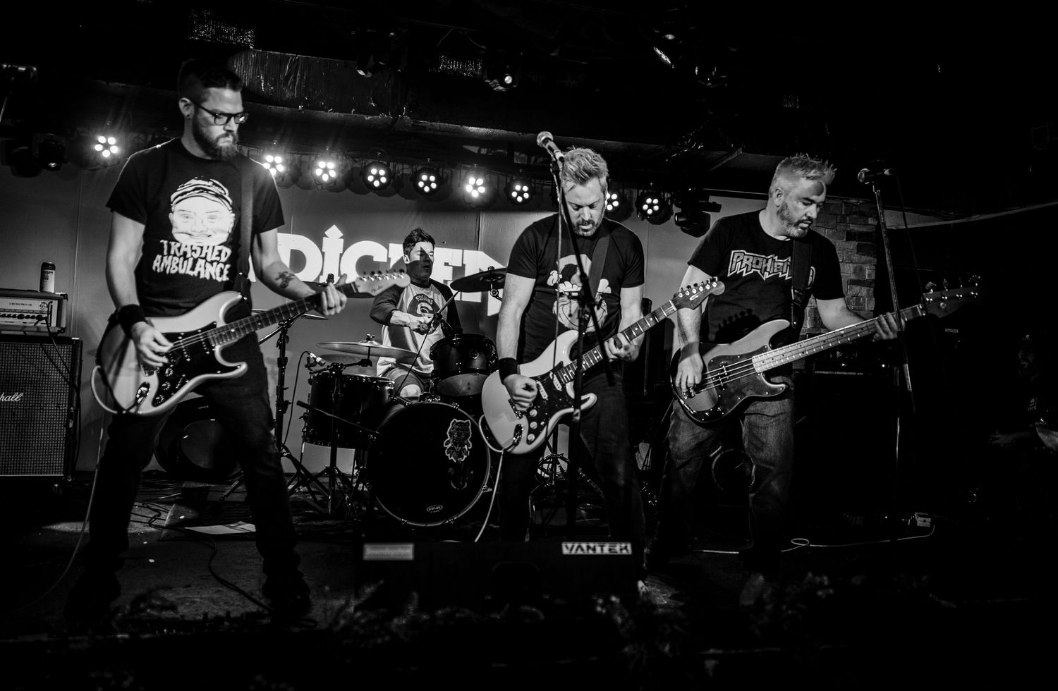 Black and white photo of a punk rock band performing on stage with dramatic lighting.