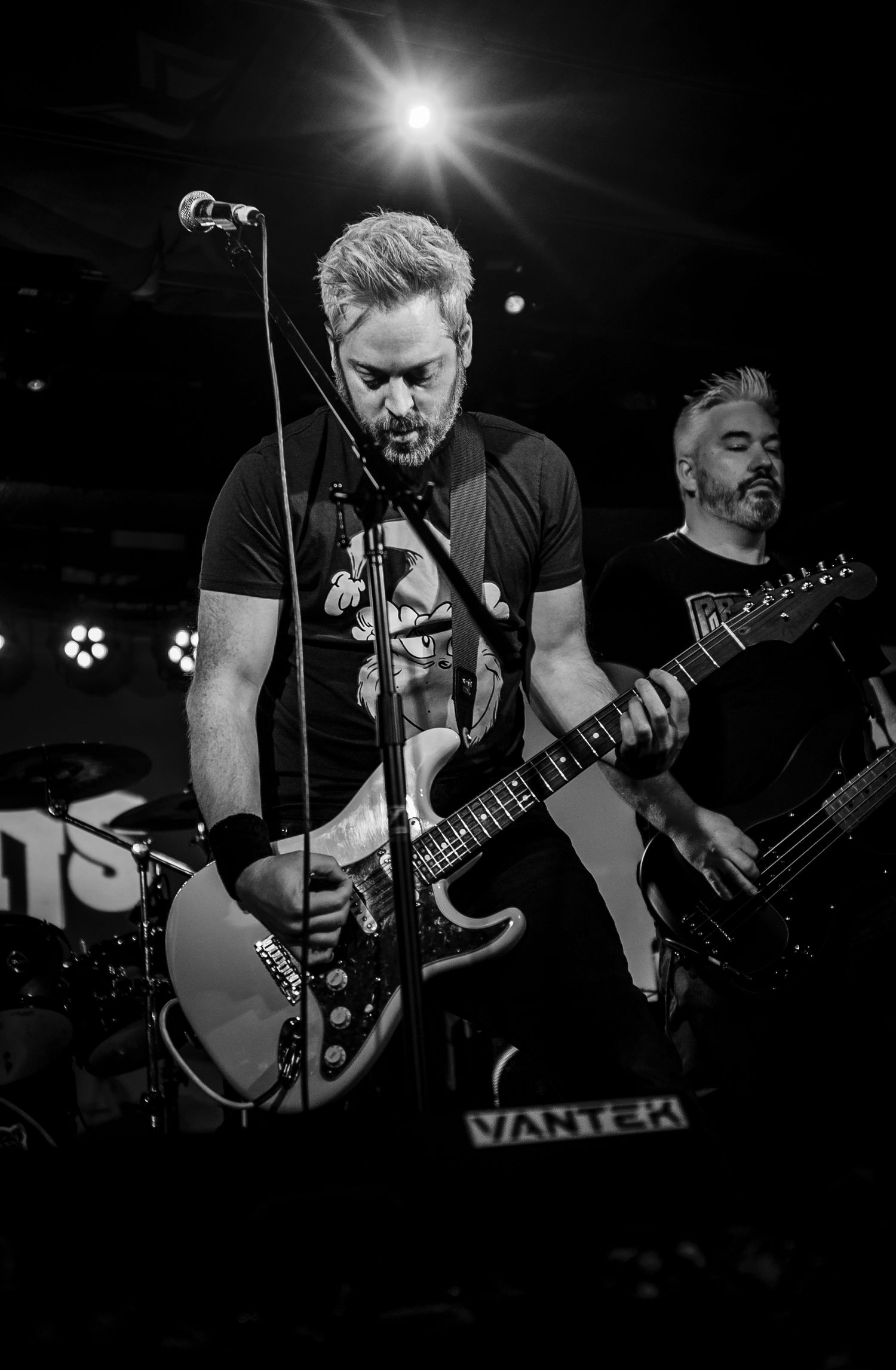 Dramatic black and white concert photo of musicians performing with bright spotlight illumination.