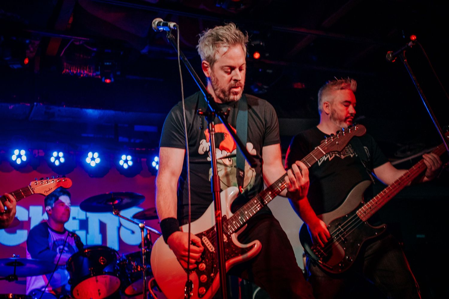 Rock band performing on stage with blue and red lighting effects.