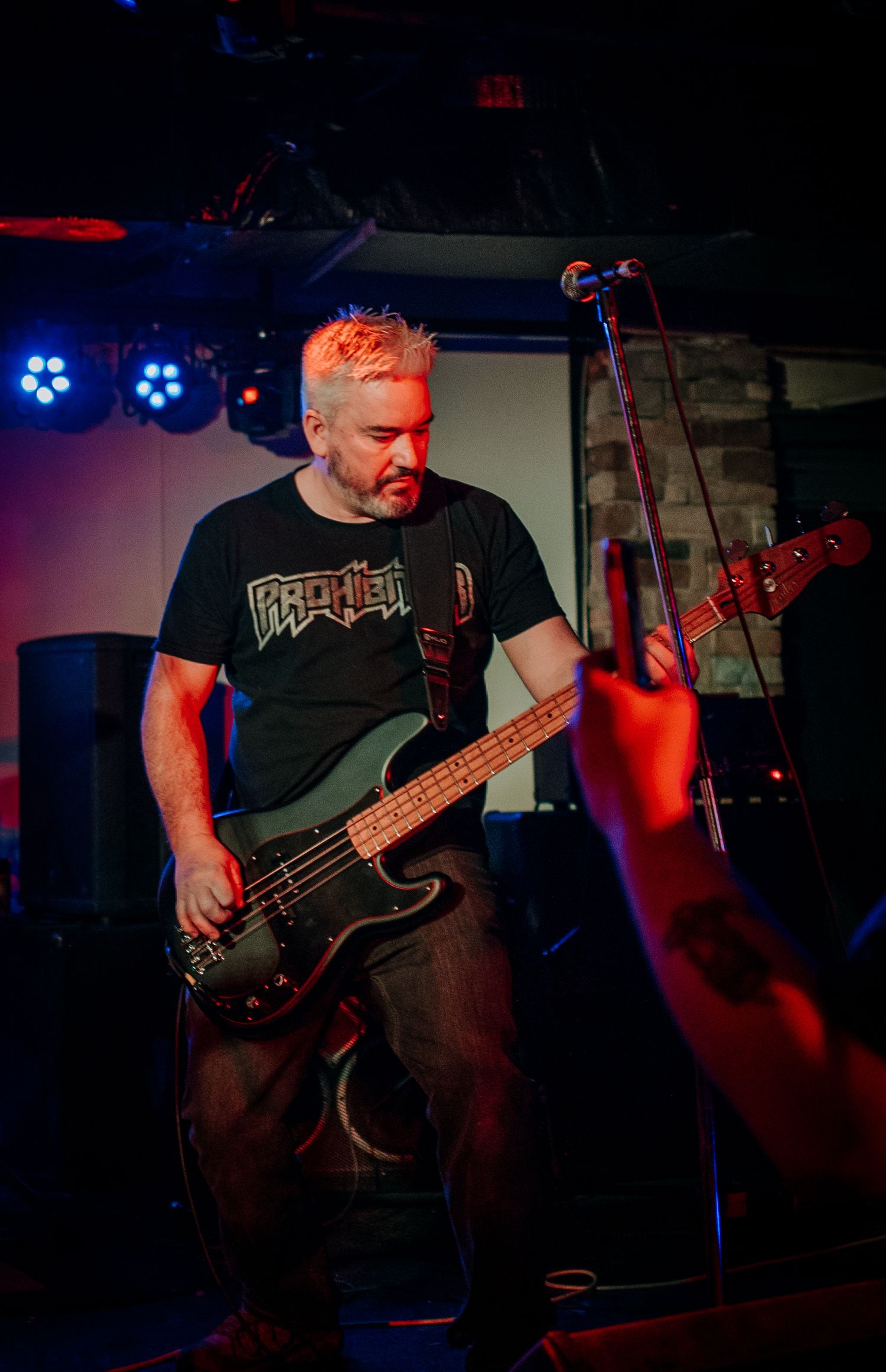 Bass player in metal band t-shirt performing on dimly lit concert stage.
