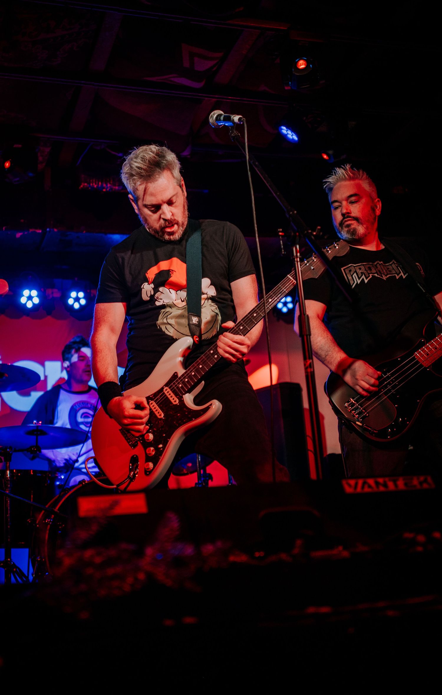 Musicians perform on stage with electric guitars under dramatic blue and red stage lighting.