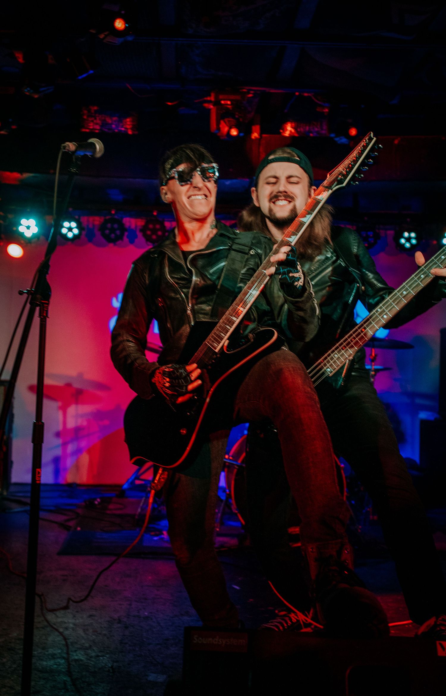 Two musicians perform together with guitars on stage under colorful lighting effects.