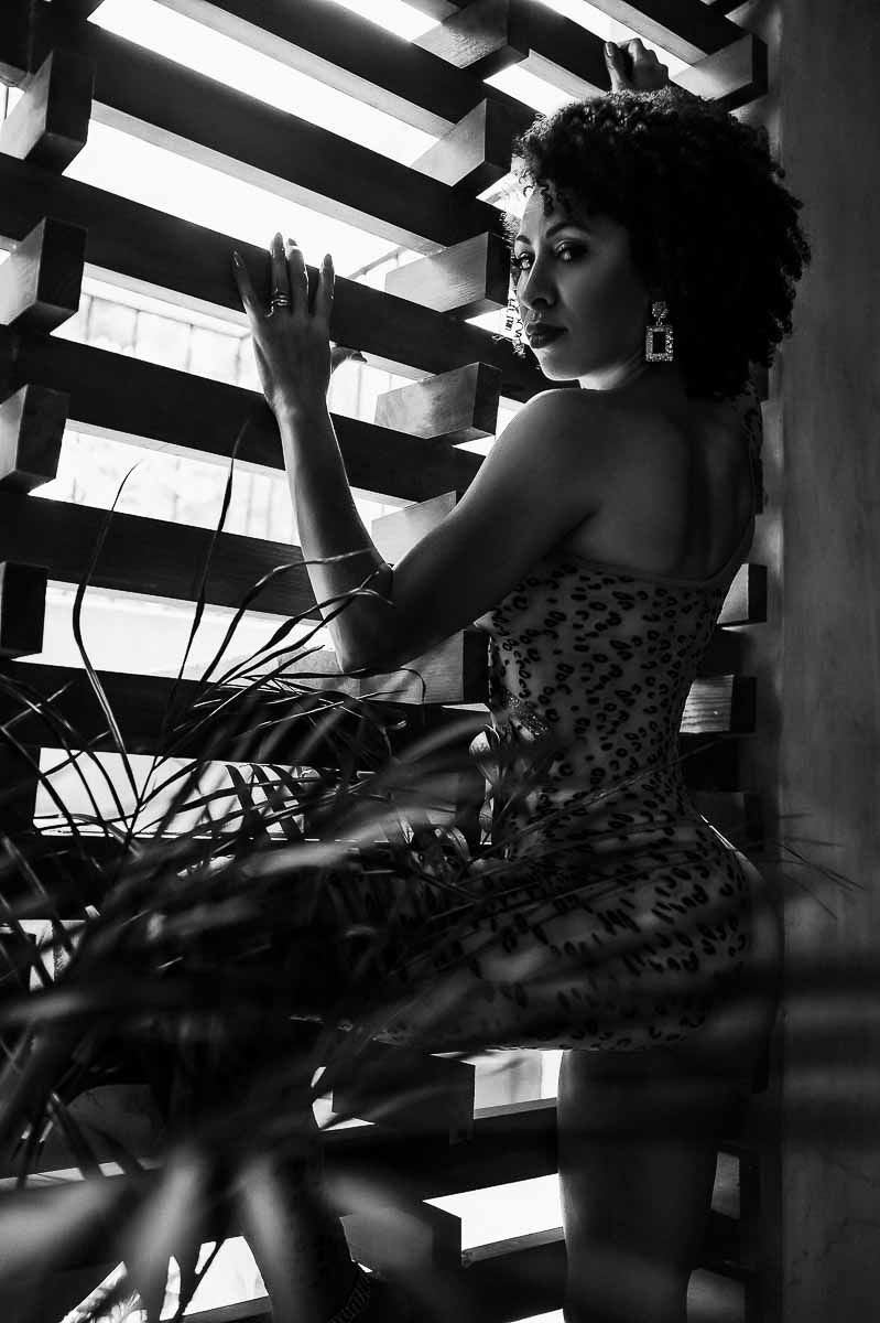 Artistic portrait through window blinds with tropical plants creating shadow patterns.