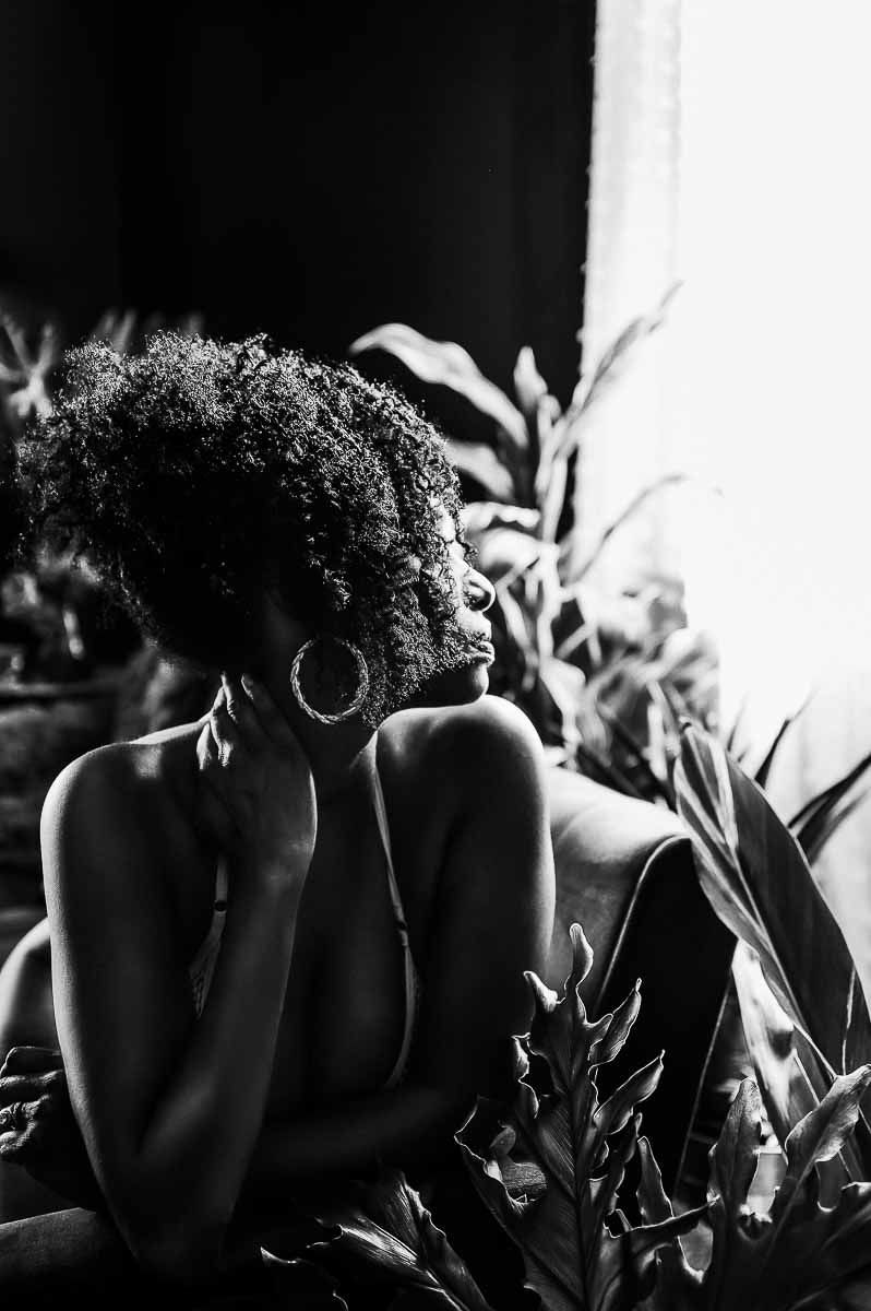 Dramatic silhouette portrait with curly hair and hoop earrings among tropical plants.