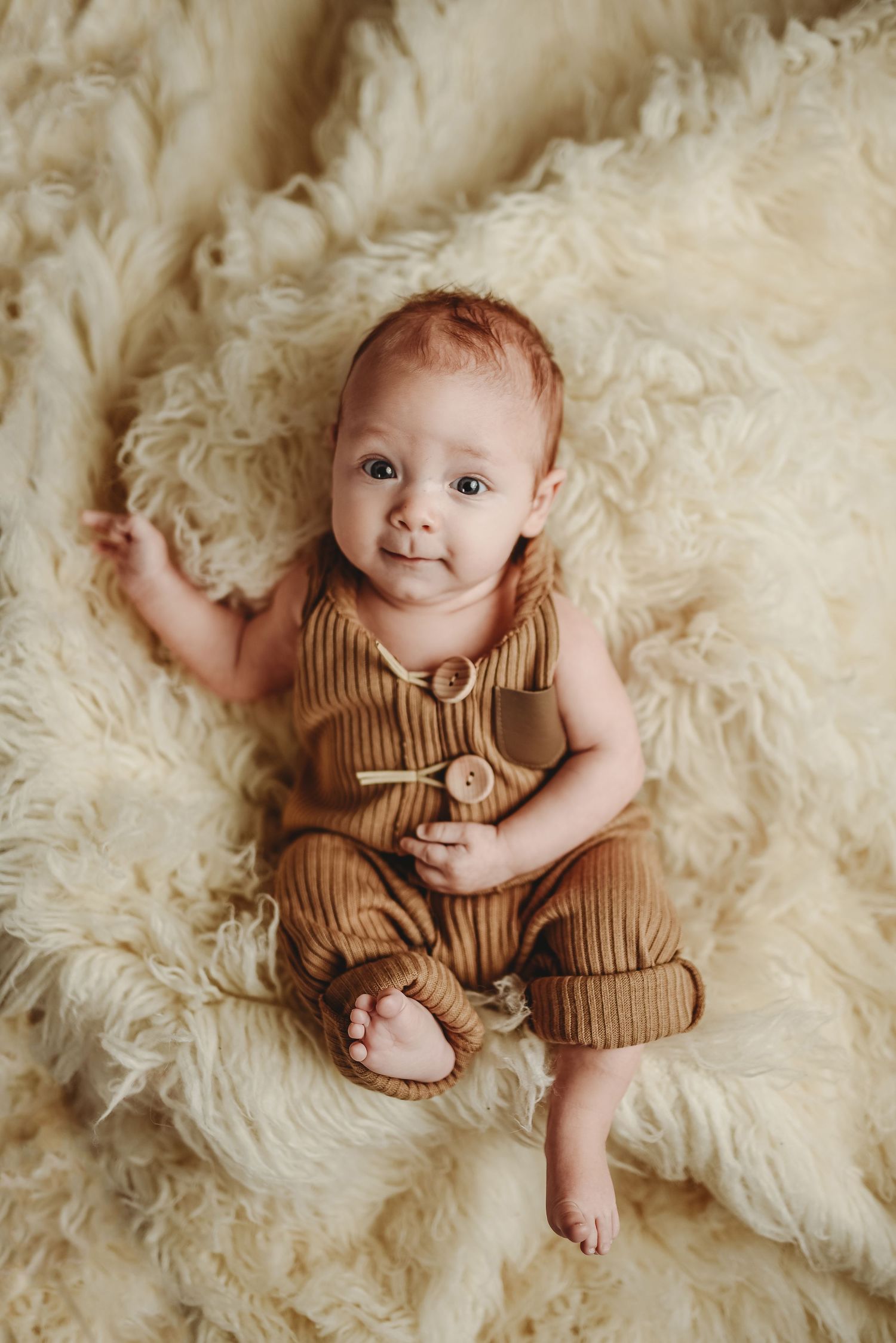 Baby in brown ribbed romper resting on soft cream colored fur blanket.