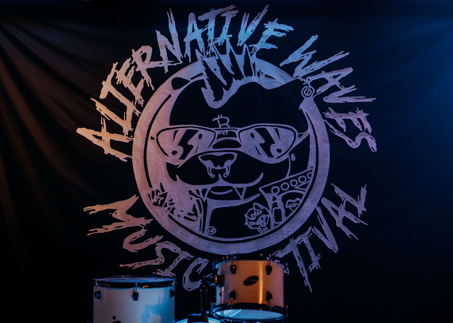 Alternative Lives circular band logo with sunglasses design illuminated on dark backdrop.