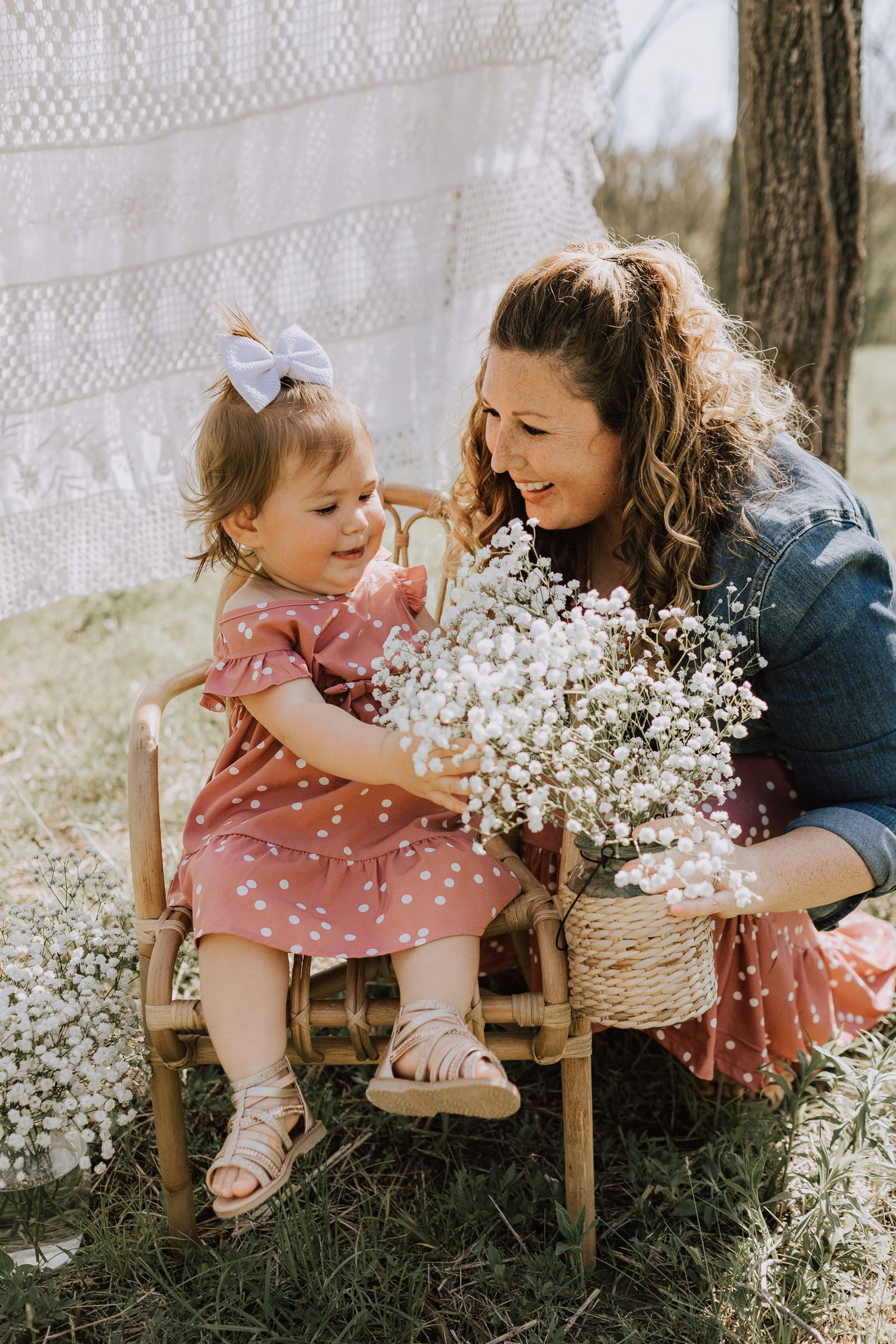 toddler girl sitting in rattan chair looking at boquet of babys breath in moms hands overland park photographer