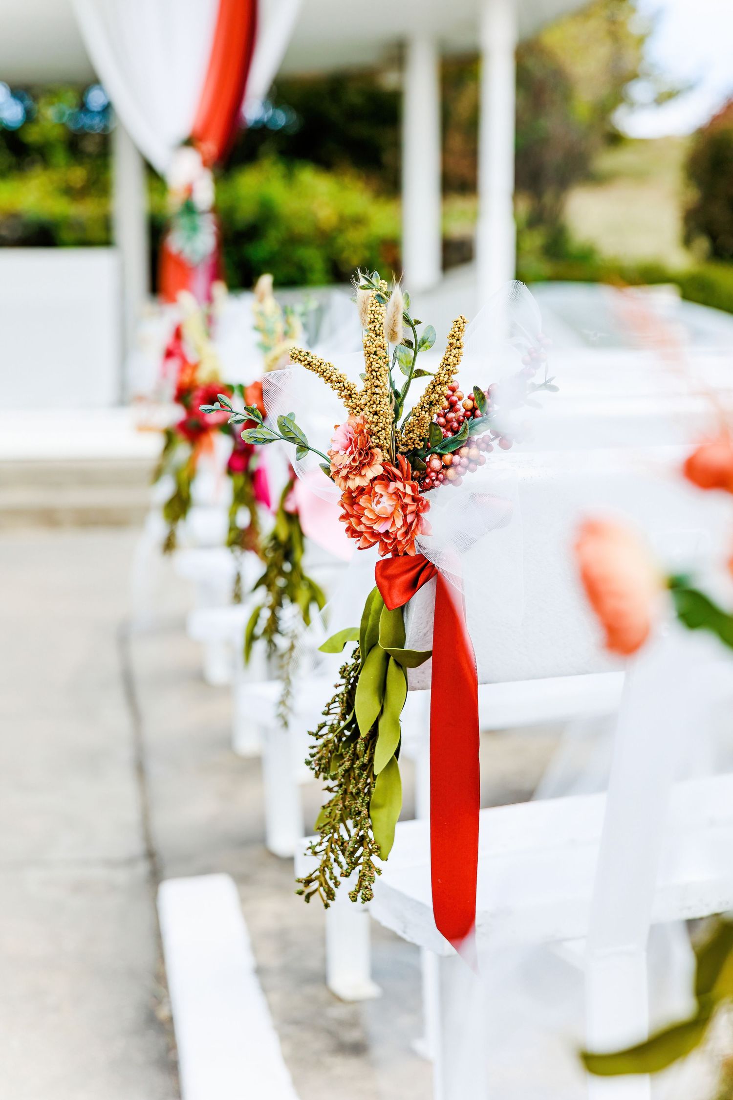 White chairs decorated with red ribbons and floral arrangements for outdoor event by Stephanie Coulter Photography