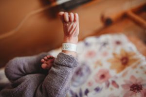 Close-up of newborn baby's hand and hospital ID bracelet against gray clothing.