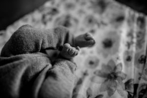Black and white close-up of newborn's tiny feet wrapped in soft blanket.