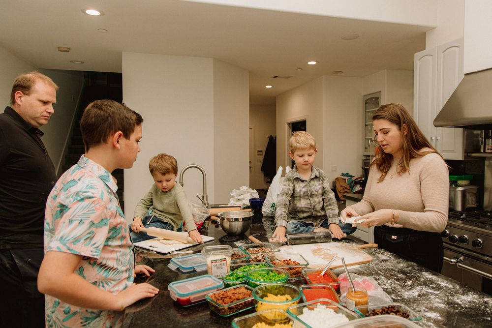 A group gathers around a kitchen counter preparing food together with ingredients and bowls laid out.