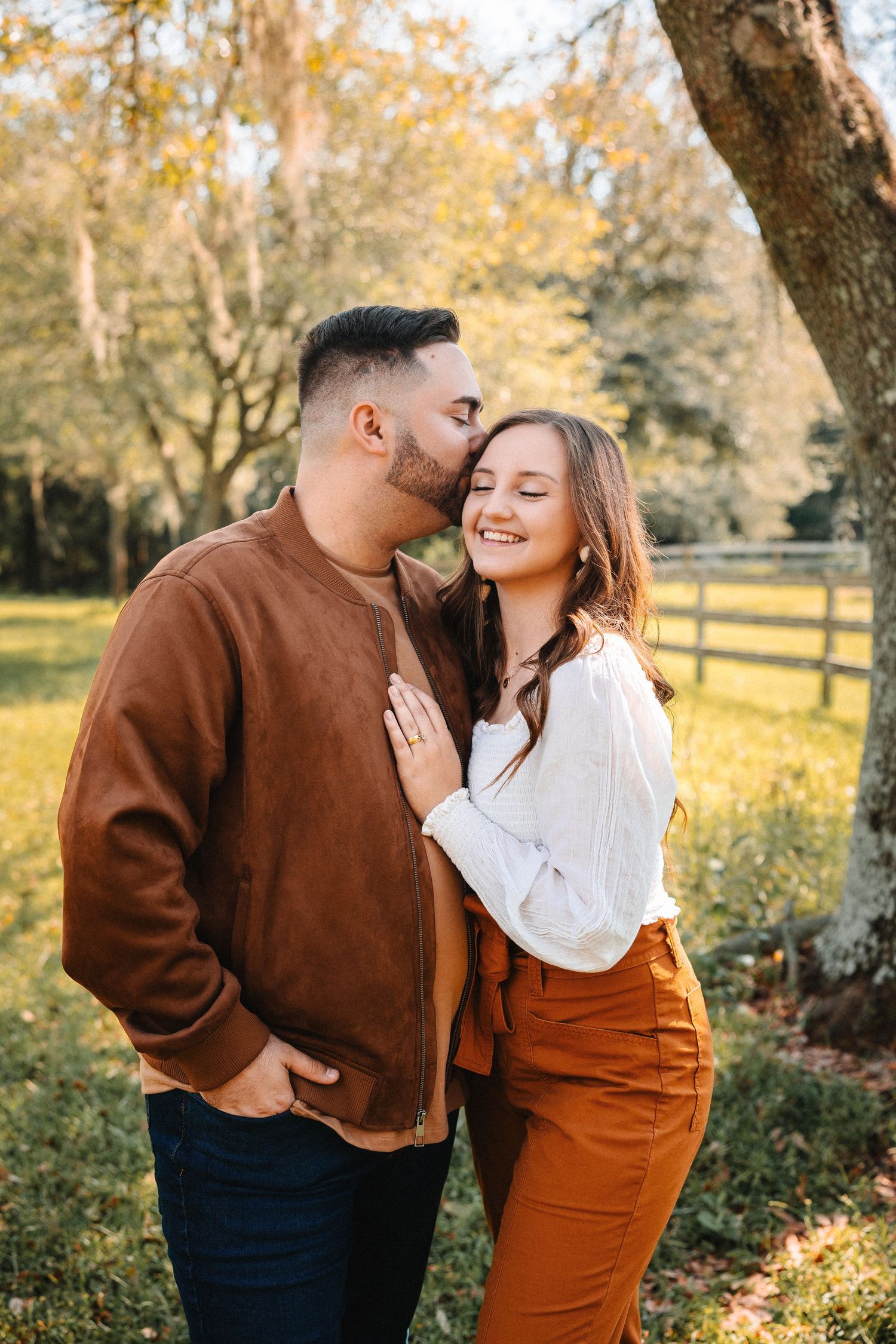 Couple sharing a tender moment outdoors, man kissing womans cheek near a wooden fence.