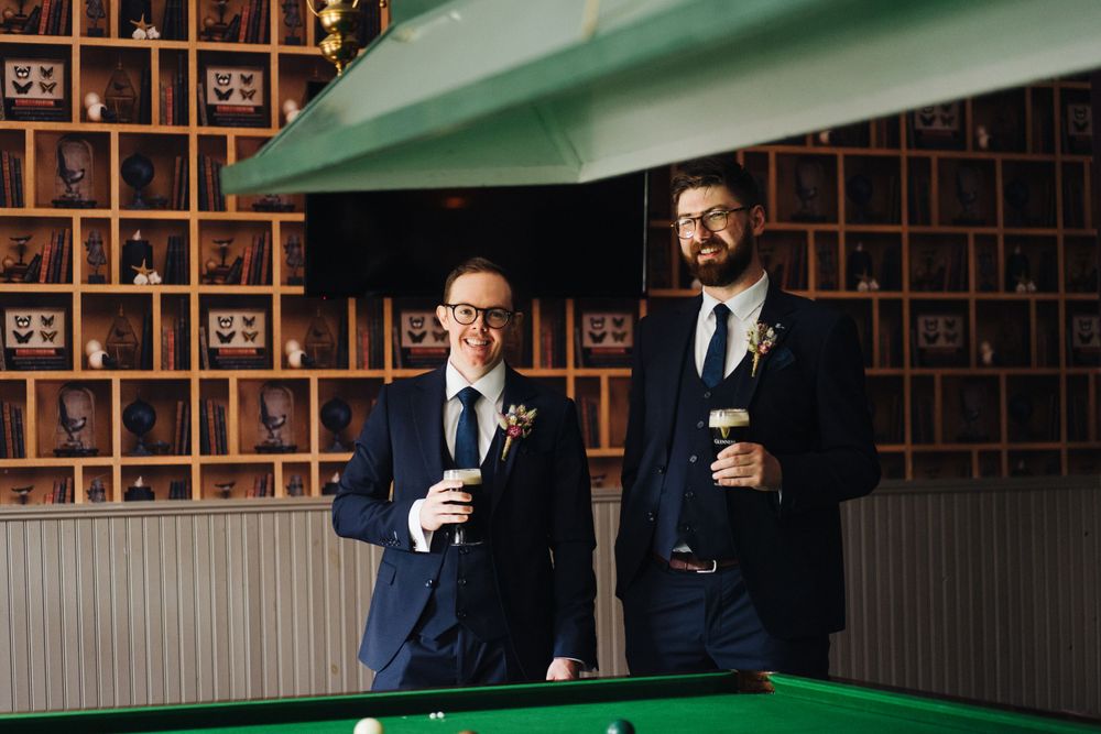 Wedding party members enjoying drinks around a pool table with decorative wall backdrop.