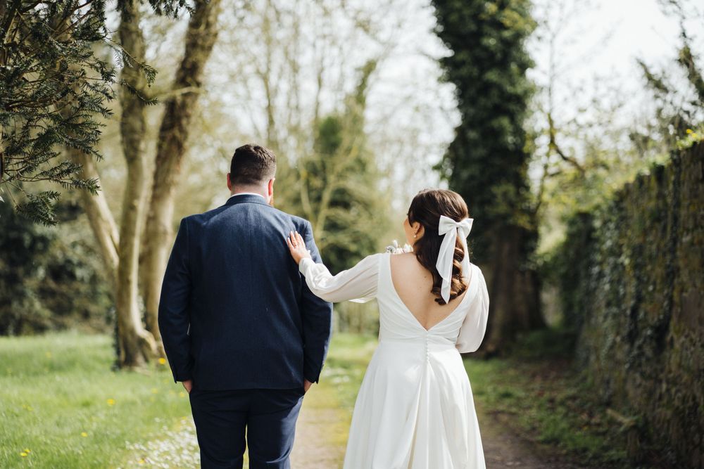 Couple strolling together on tree-lined path during wedding photo session.