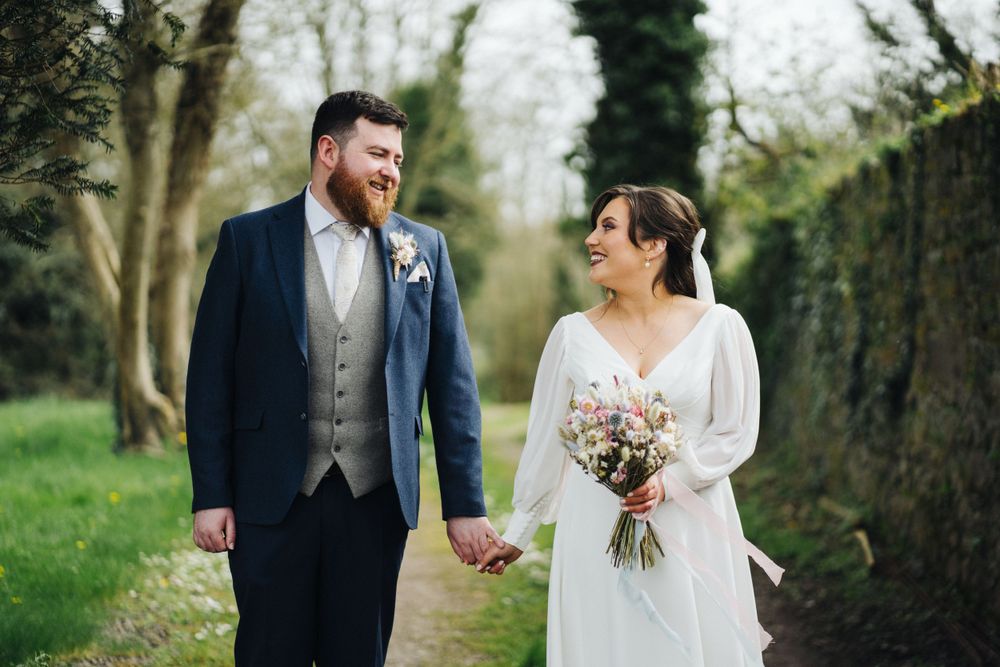 A happy couple exchanges loving glances while walking hand in hand on their wedding day.