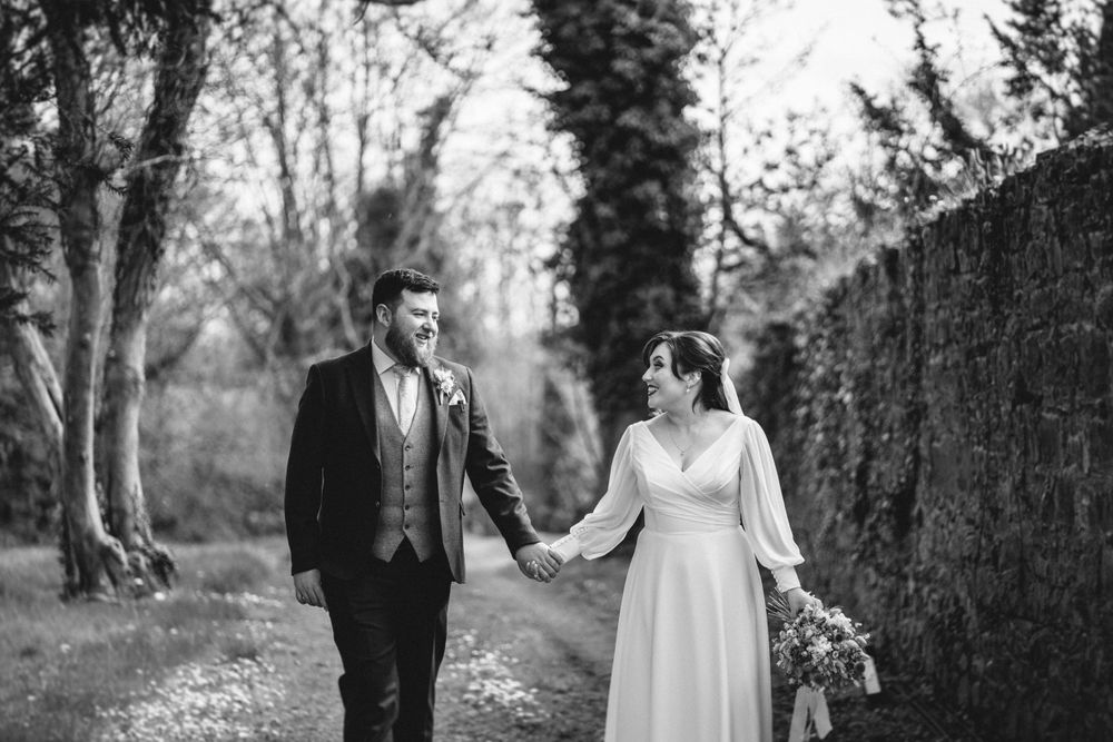 A black and white photo captures a romantic moment between newlyweds on a garden path.