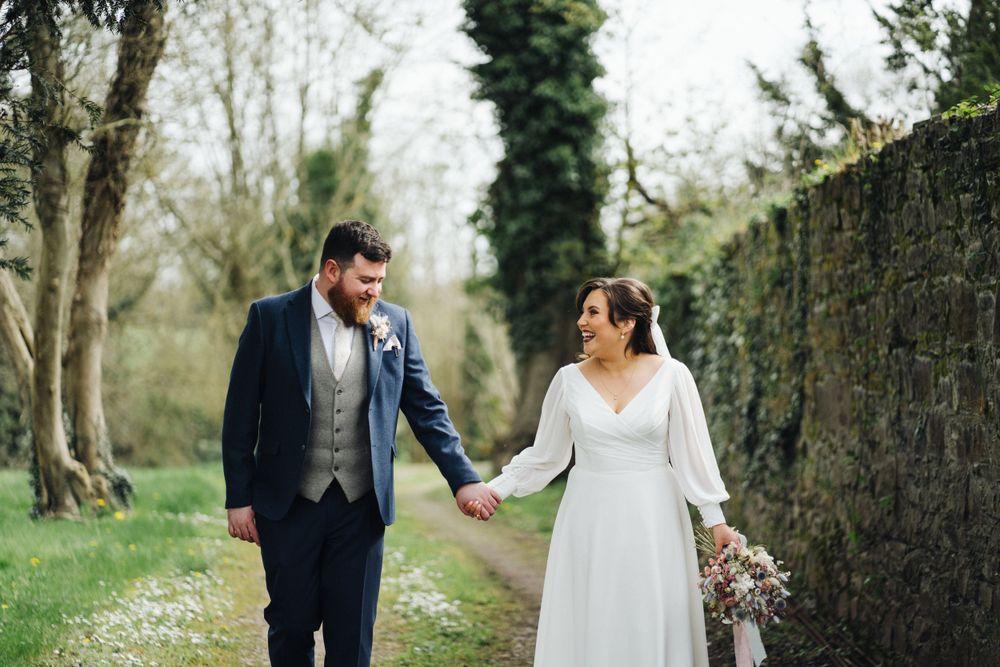 A couple shares an intimate moment while walking along an ivy-covered garden wall.