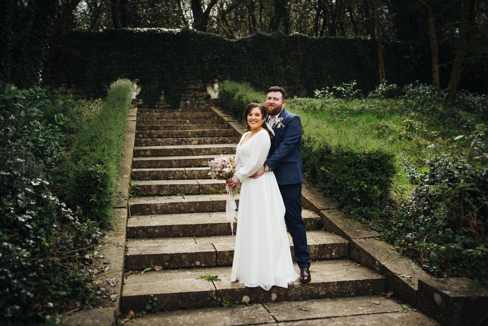 A couple shares a romantic moment on historic stone steps surrounded by hedges and greenery.
