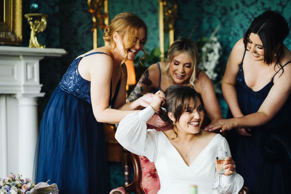 Wedding party helps with final dress adjustments in an elegant room with ornate decor.