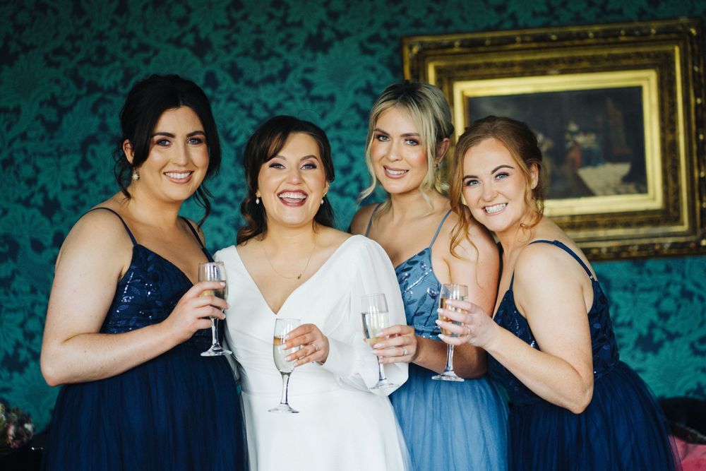 Wedding party raises champagne glasses for a toast against a teal patterned wall.
